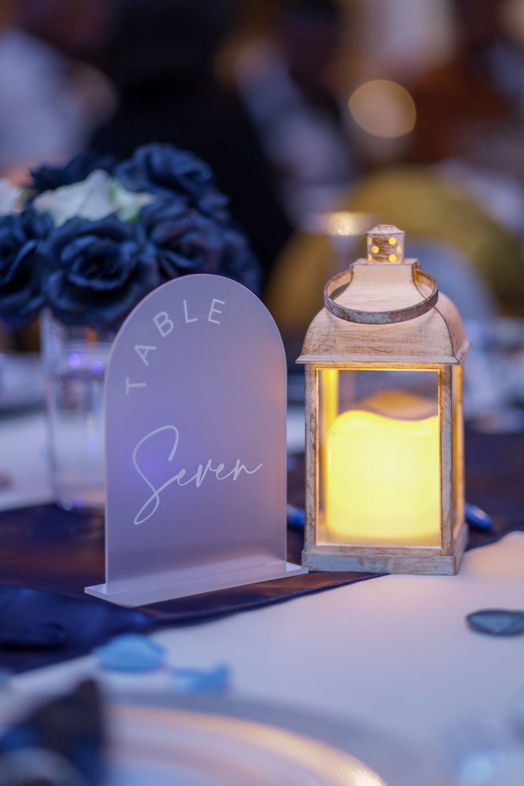 Guests seated around a U-shaped table with candles, greenery, and balloon backdrop in green, cream, and gold.
